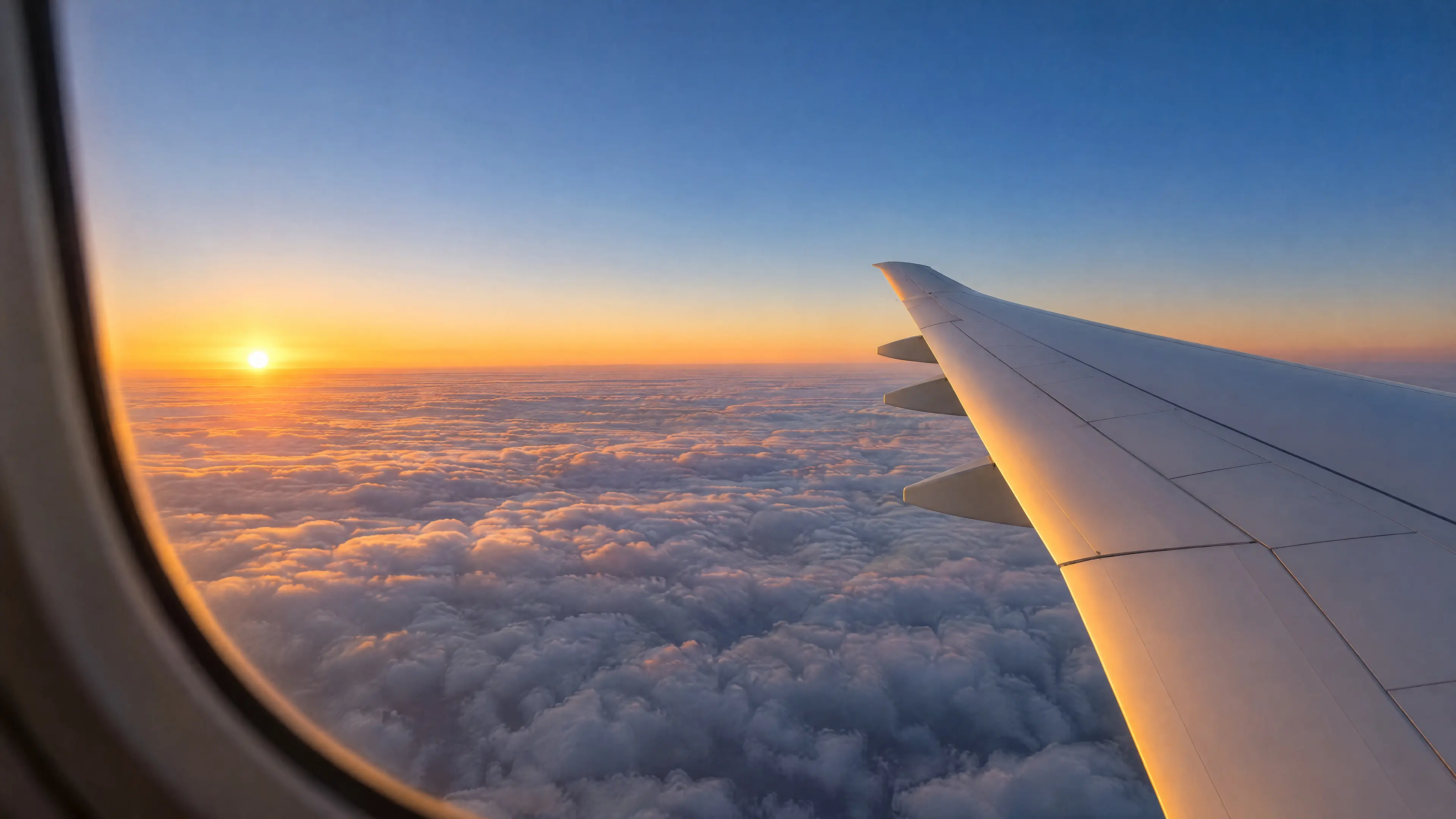 The view from a window seat at sunrise: a white wing over a flat sea of cloud